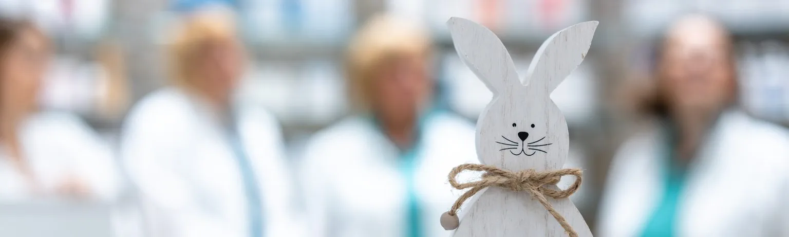 Weißer Deko-Hase vor unscharfem Apothekenteam im Hintergrund
