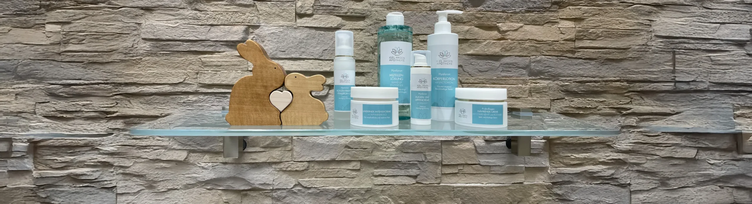 Hautpflegeprodukte der Igel Hasen Apotheke mit Holzhasen-Deko auf Glasregal vor Steinwand