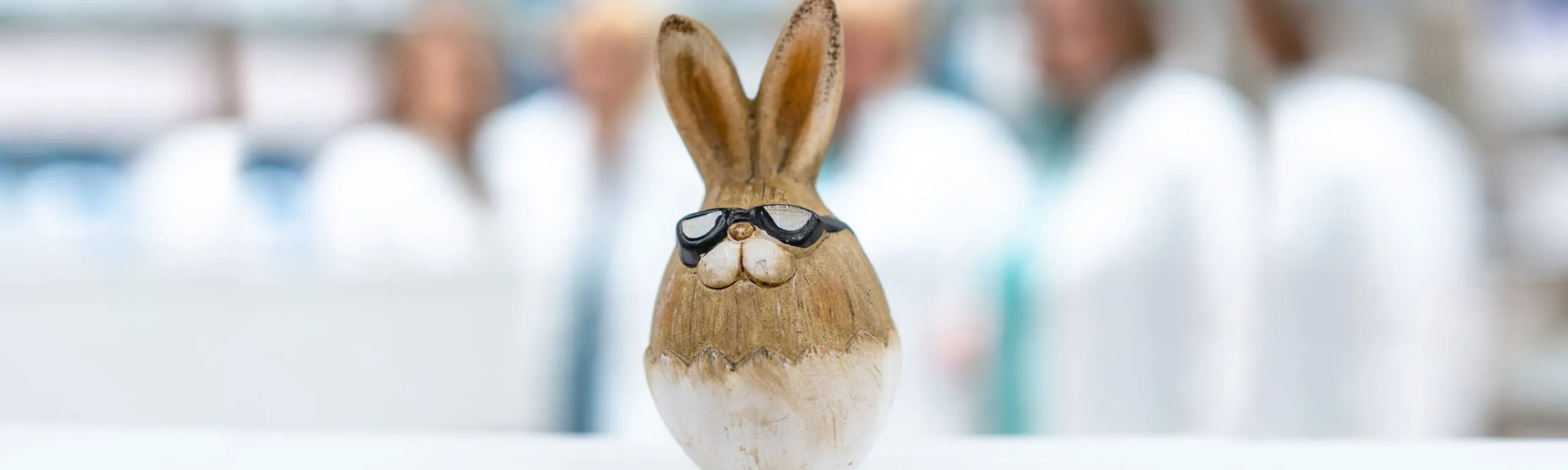 Deko-Hase mit Sonnenbrille vor unscharfem Team der Igel-Hasen-Apotheke im Hintergrund